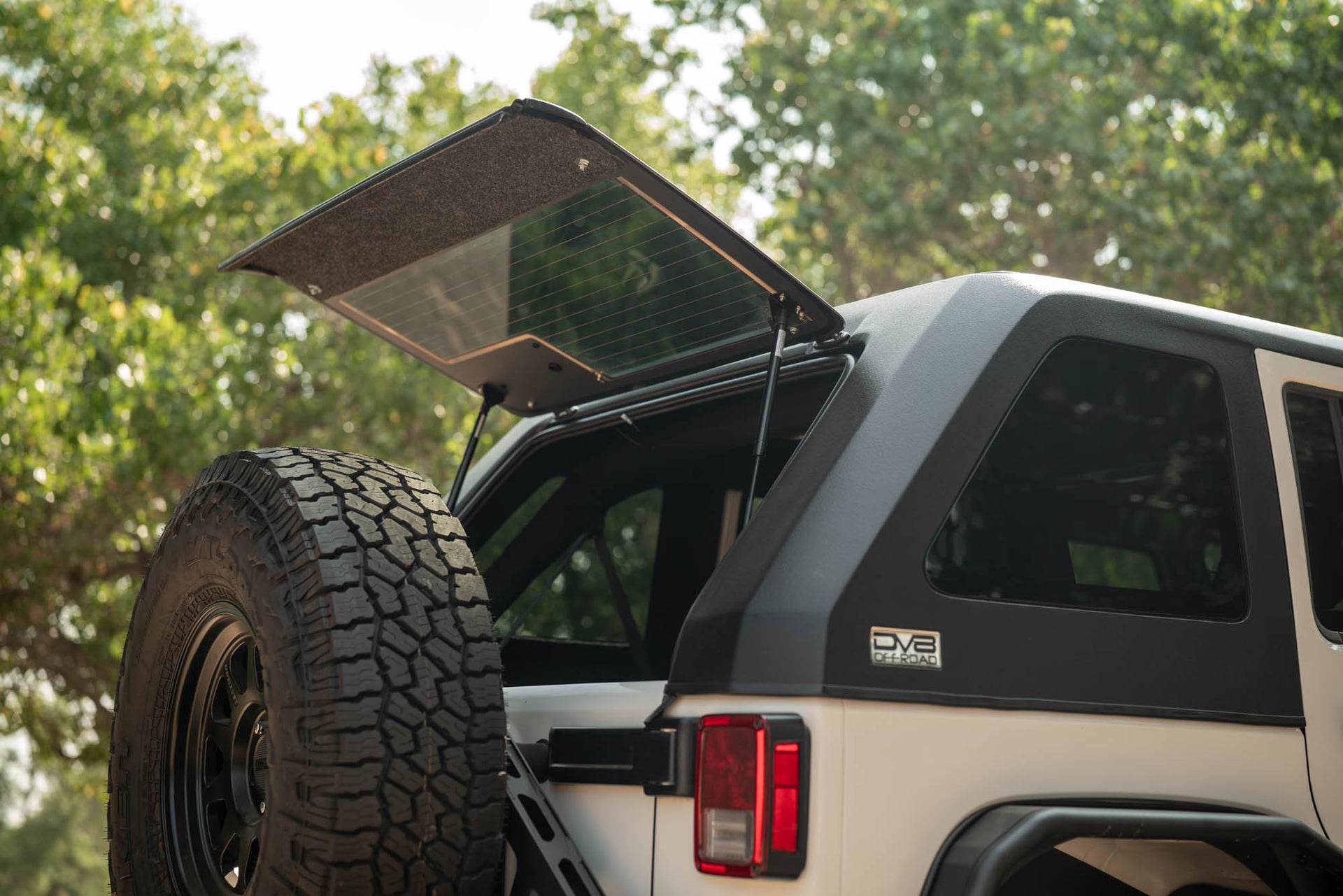 White 2007-2018 Jeep JK 4-Door with DV8 Fastback Hard Top with open rear window and tire in a natural setting