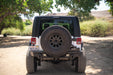 Back view of a 2007-2018 Jeep JK 4-Door with DV8 Square Back Hard Top on a dirt road with trees and bushes in the background.