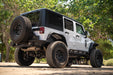 White 2007-2018 Jeep JK 4-Door with DV8 Square Back Hard Top with large tires on a dirt road surrounded by trees