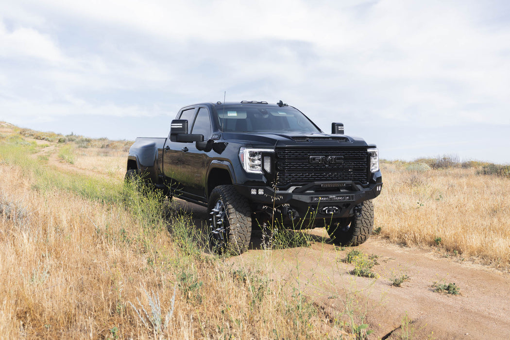 Spec Series Front Bumper for the 2020-2023 GMC Sierra 2500/3500 on a dirt road with grassy landscape and cloudy sky
