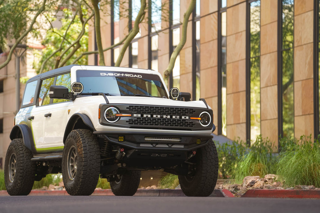 White Ford Bronco with off road parts parked in an urban setting with trees and buildings in the background