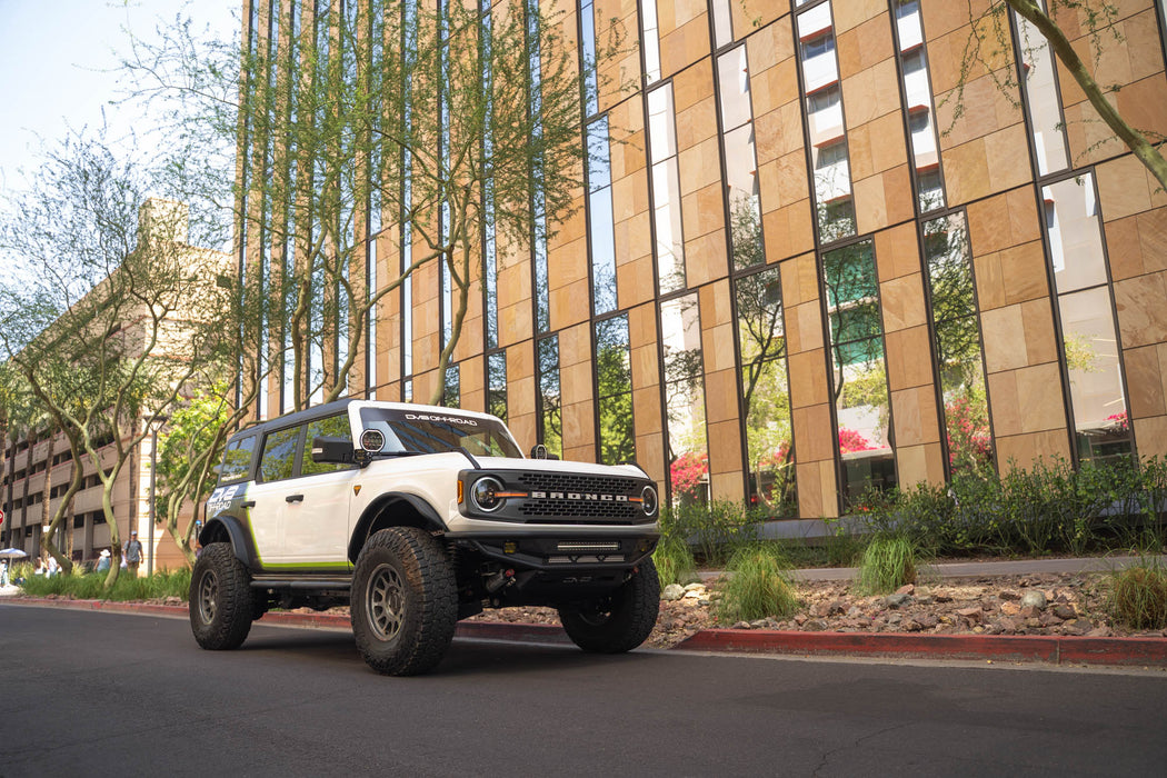 White Ford Bronco with off road parts parked in front of a modern building with glass facade