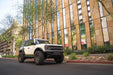 White Ford Bronco with off road parts parked in front of a modern building with glass facade