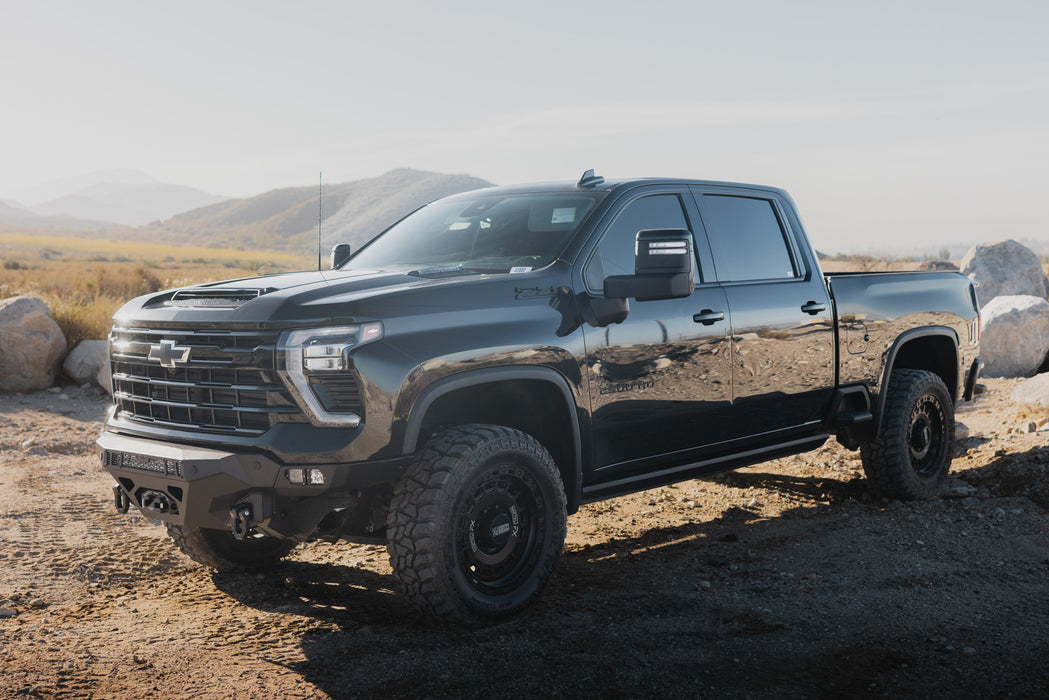 Black 2024-2026 Chevy Silverado 2500/3500  with our Spec Series Front Bumper parked on a dirt road with mountains in the background