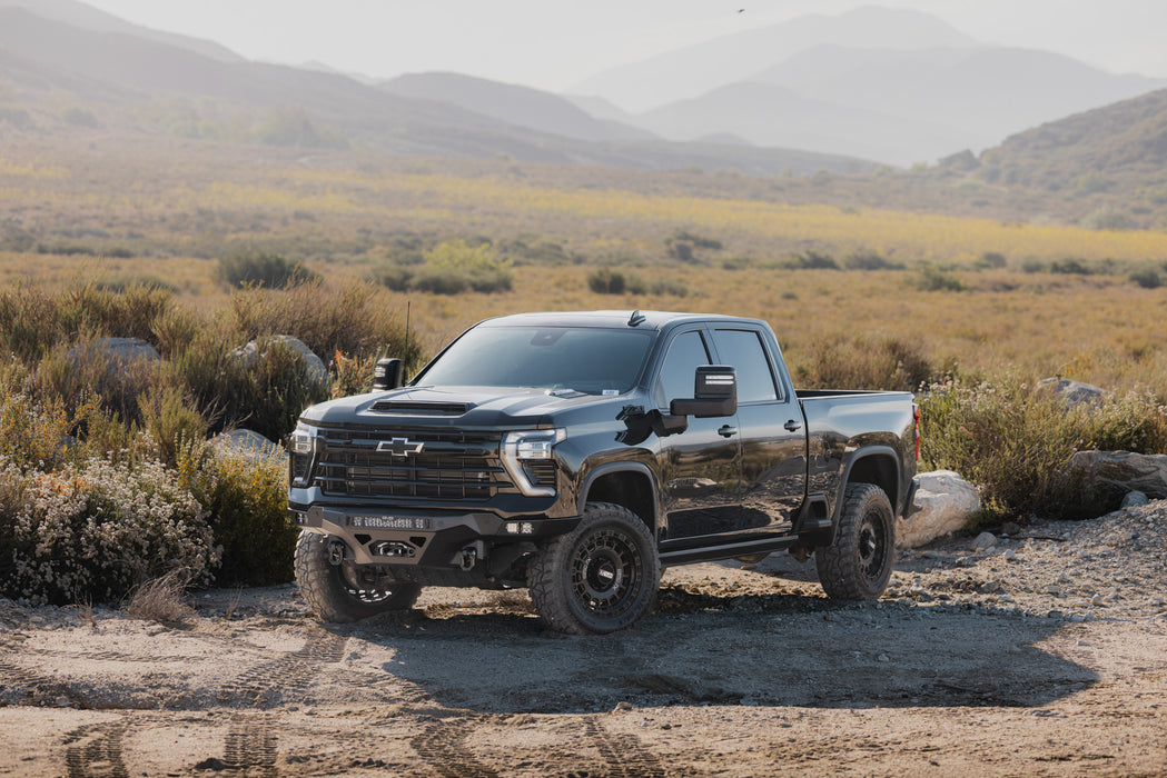 2024-2026 Chevy Silverado 2500/3500  with our Spec Series Front Bumper parked in dirt lot with valley of brush and boulders behind.