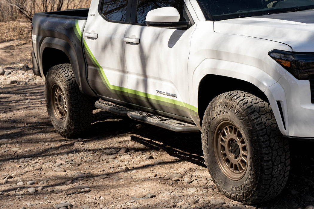 Tacoma with off road parts driving up a shaded dirt road.