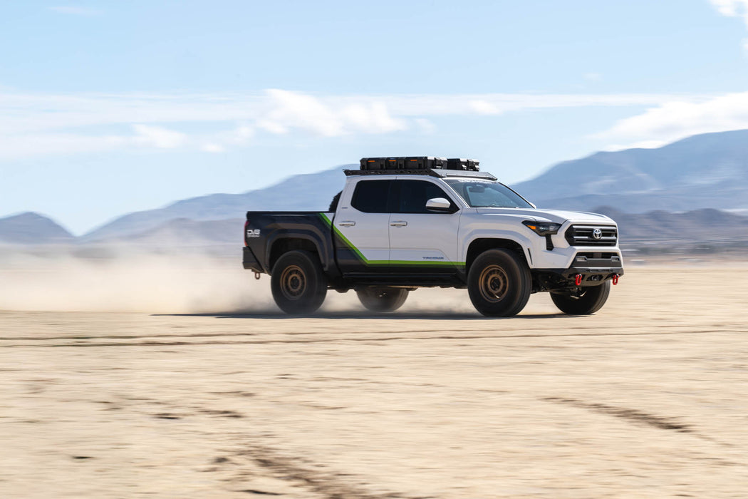 DV8 Offroad Tacoma driving on a desert road with mountains in the background.