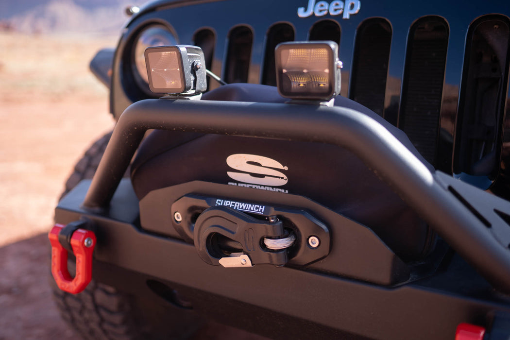 Close-up of a Jeep bumper with additional lights and a tow hook, featuring the Jeep logo.