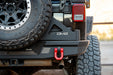 Close-up of a Jeep with a DV8 bumper and tire carrier, set against a blurred natural background.