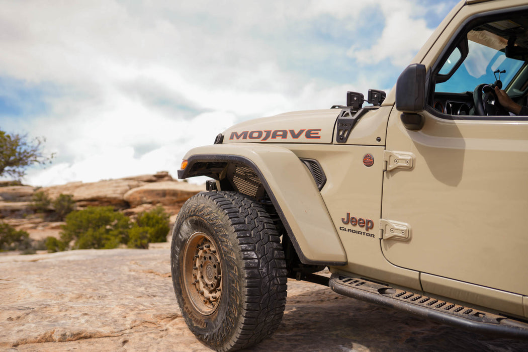 Beige Jeep Wrangler Mojave edition parked on a rocky landscape with a clear sky.