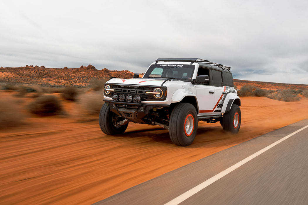 White Ford Bronco Raptor with Tube Front Bumper with red accents driving on a desert road.