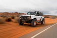 White Ford Bronco Raptor with Tube Front Bumper with red accents driving on a desert road.